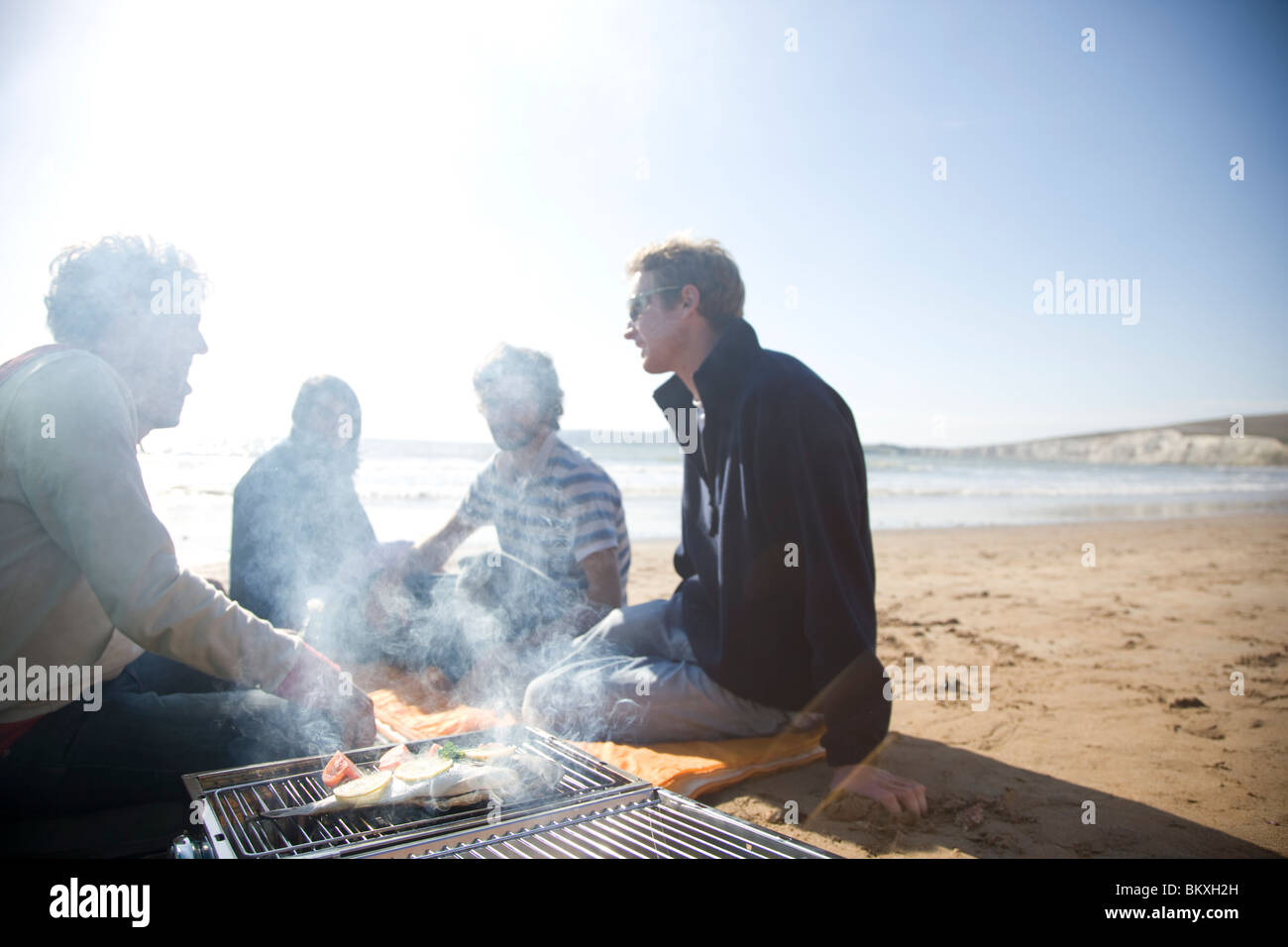 Groupe d'amis assis autour d'un barbecue sur la plage Banque D'Images