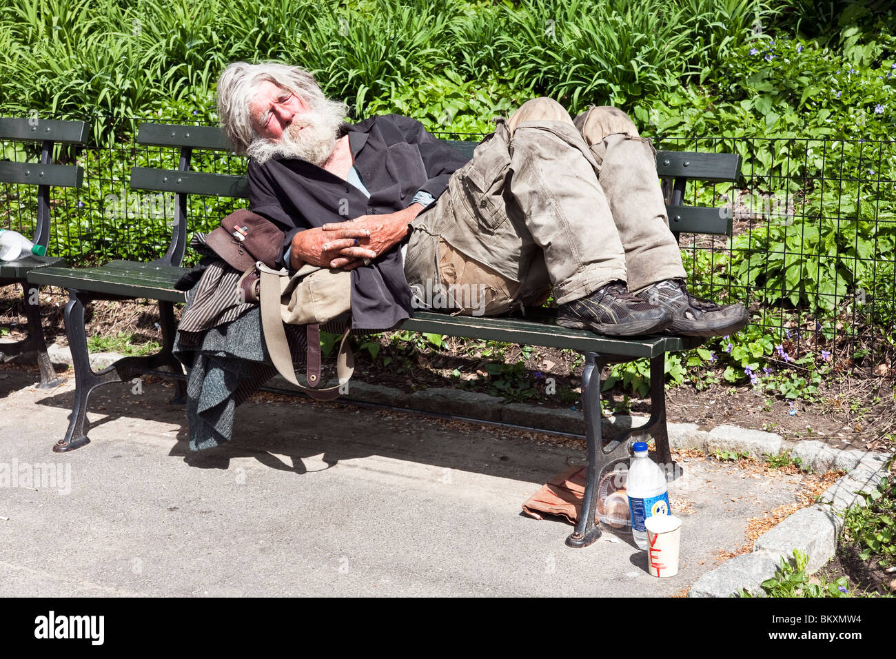 Vieux lambeaux de vêtements sales d'EFP bénéficie du soleil de printemps sur un banc dans Central Park à New York City Banque D'Images