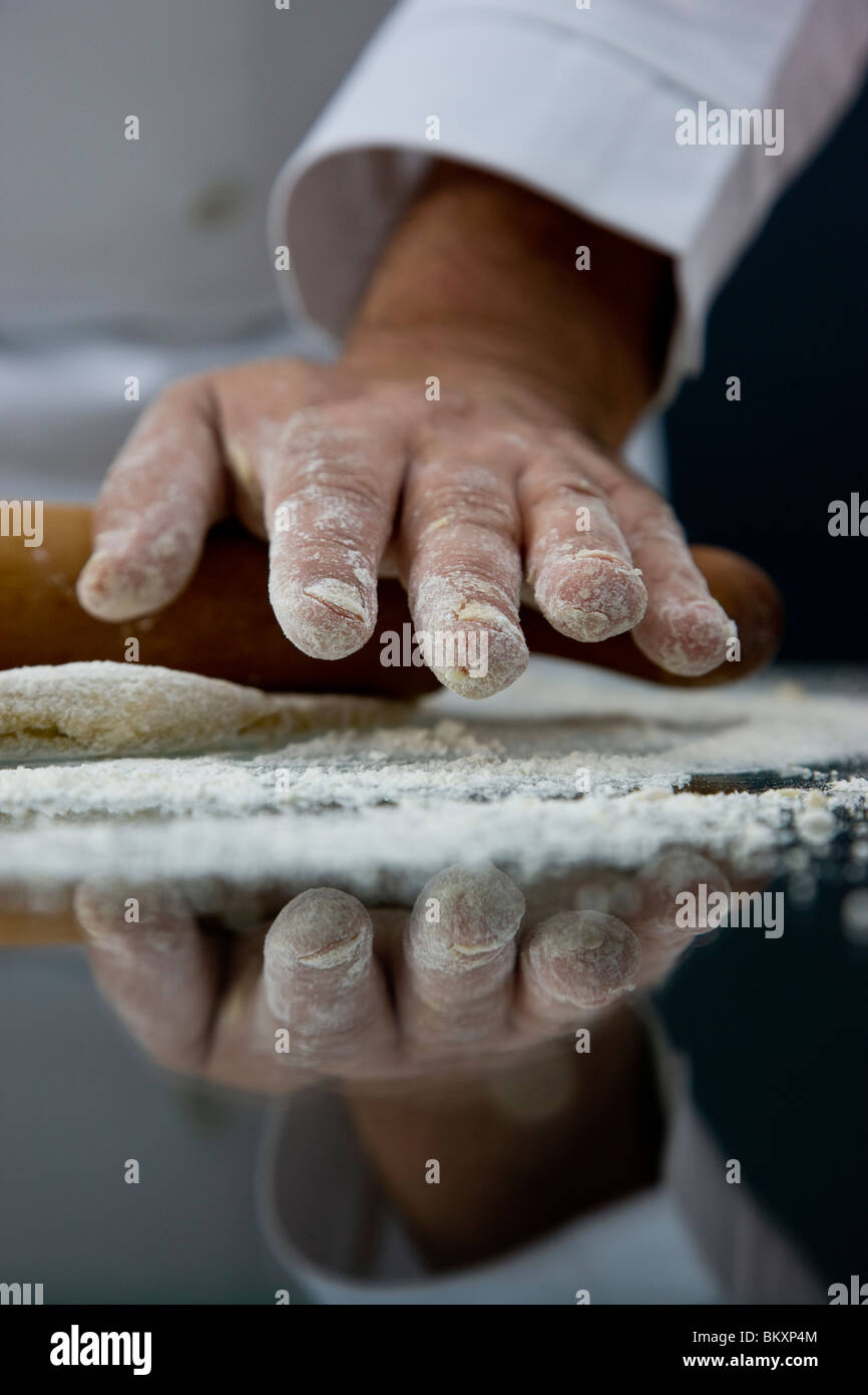 Close up of a chef part couvert de farine le roulement d'un rouleau à pâtisserie sur un la pâte sur une table en verre Banque D'Images