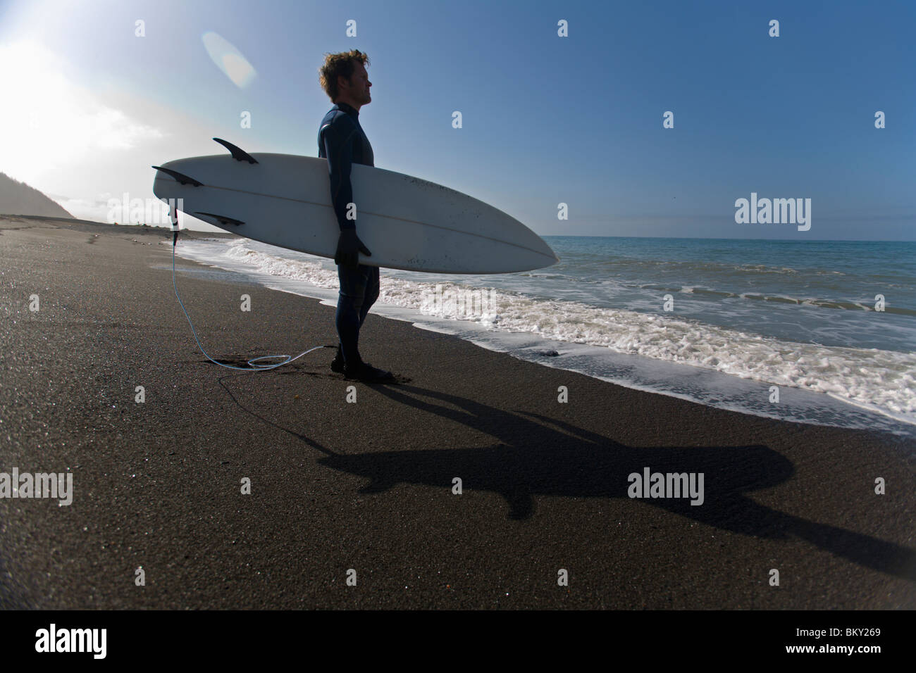 Un homme se tient sur la plage avec une planche de surf sous le bras sur la Lost Coast, Californie. Banque D'Images