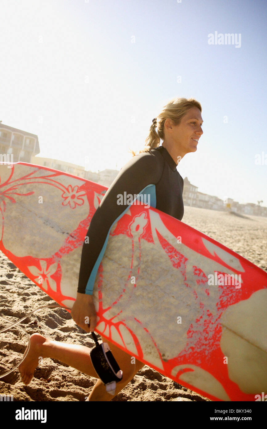 Une femme sur un matin ensoleillé à Pacific Beach fonctionne à l'eau tenant son surf. Banque D'Images Une femme sur un matin ensoleillé à Pacific Beach fonctionne à l'eau tenant son surf. Banque D'Images