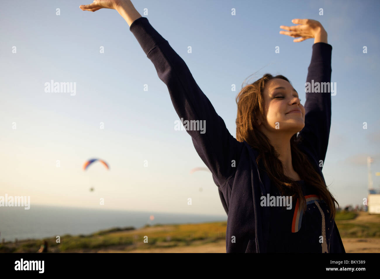 Femme dans la jeune vingtaine, jette son bras et ferme les yeux pour sentir le vent à un port de parapente en Californie. Banque D'Images Femme dans la jeune vingtaine, jette son bras et ferme les yeux pour sentir le vent à un port de parapente en Californie. Banque D'Images