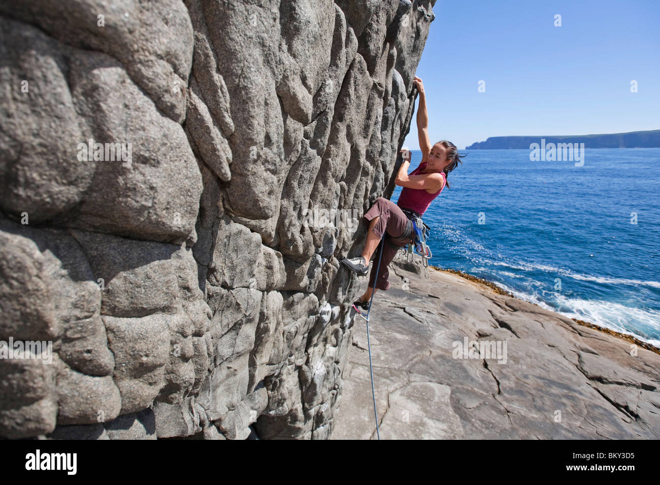 Une femme est une escalade de rocher sur la péninsule de Tasman, Tasmanie, Australie. Banque D'Images
