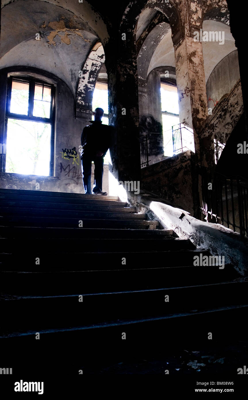 Silhouette d'un homme debout sur certains vieux escaliers dans un grand bâtiment abandonné Banque D'Images