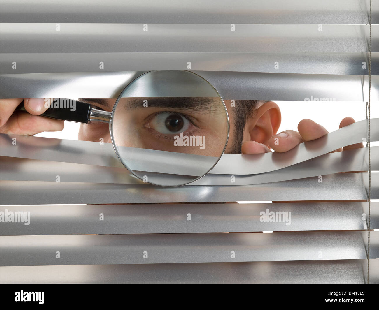 L'homme est un voyeur à travers les blinds avec une loupe. Banque D'Images