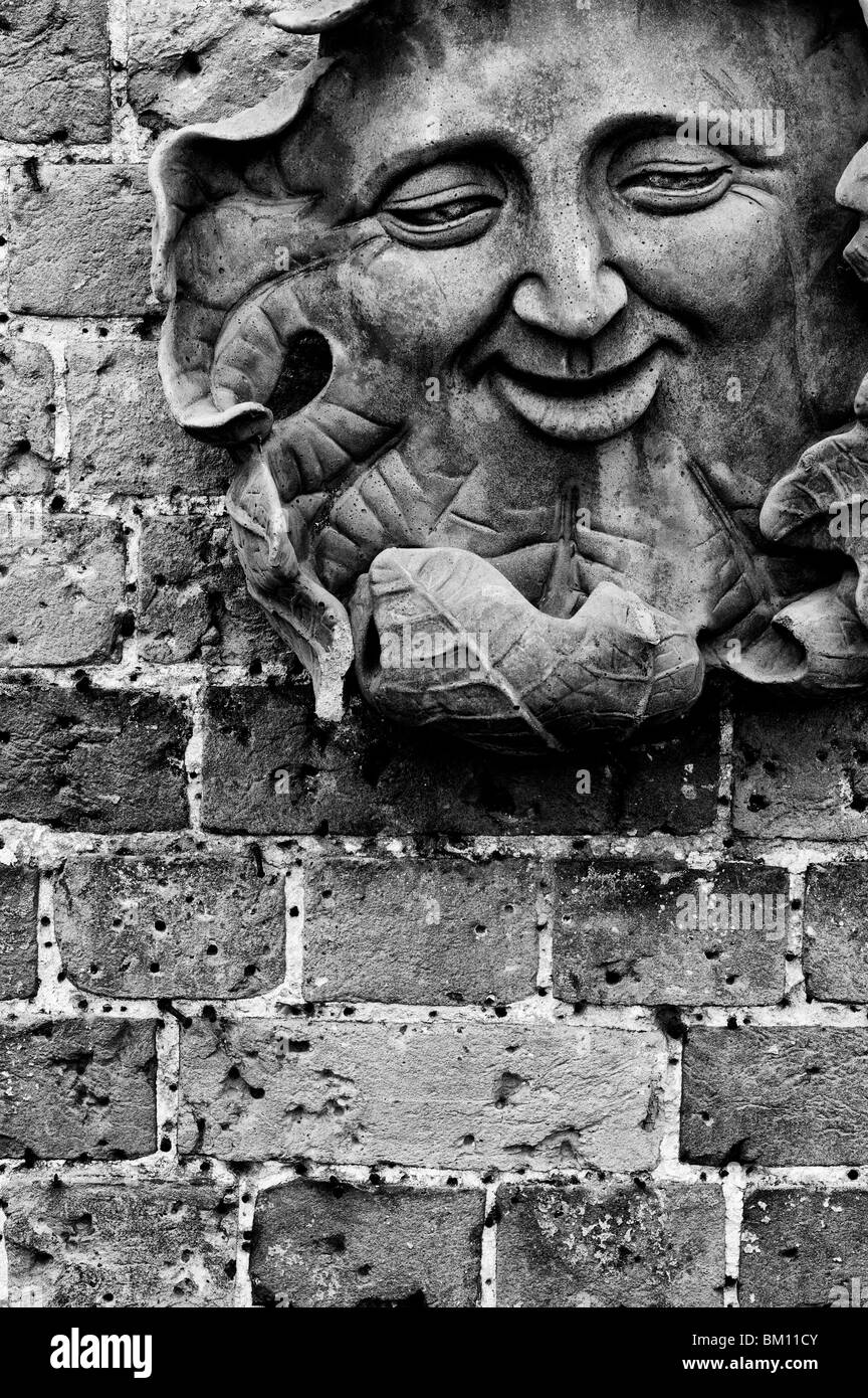 Un homme vert sculpté plaque sur un mur de jardin. Monochrome Banque D'Images