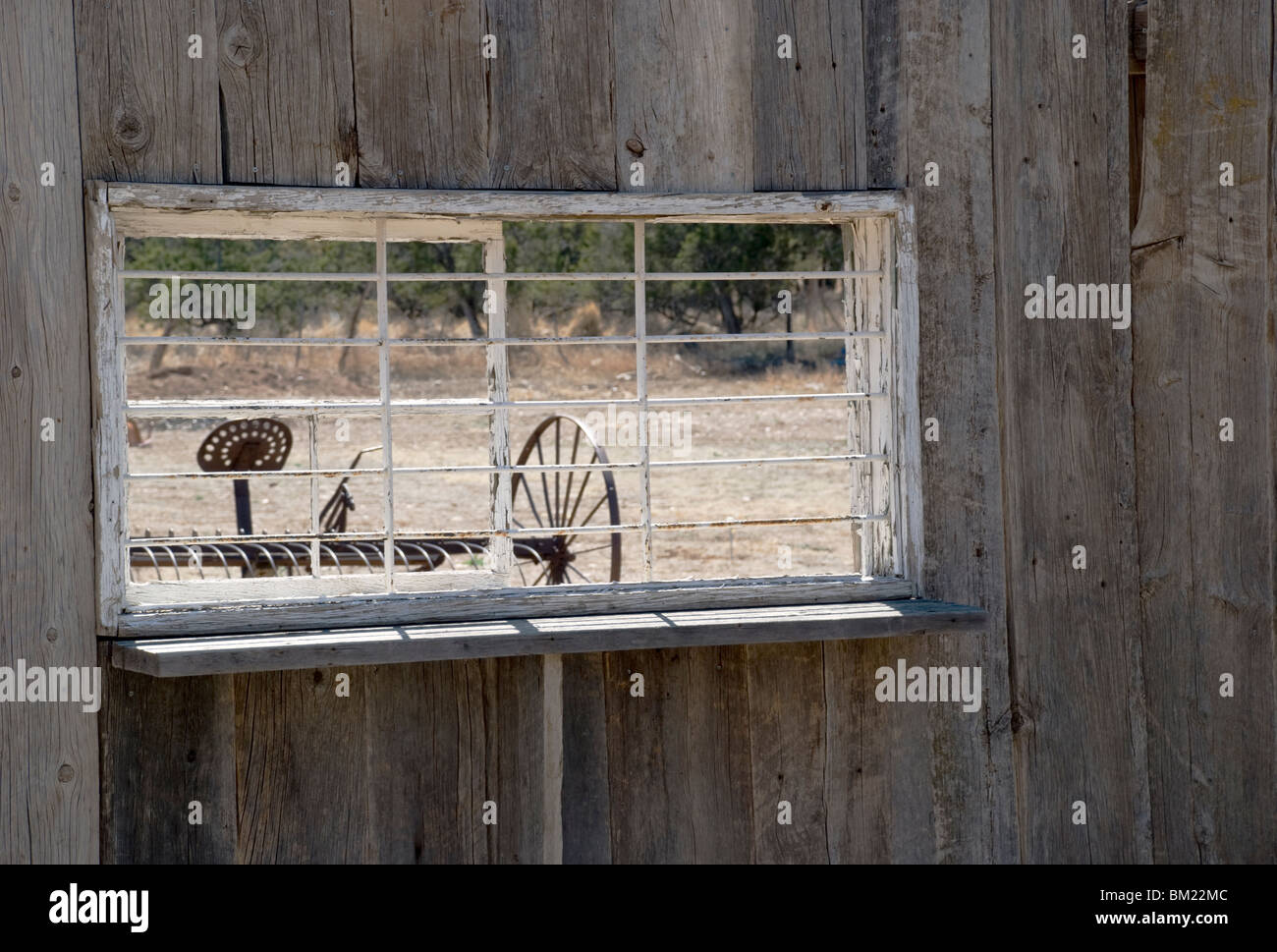 Old farm machinery est vu à travers une fenêtre ancienne dans la ville historique de Lincoln, New Mexico, USA. Banque D'Images