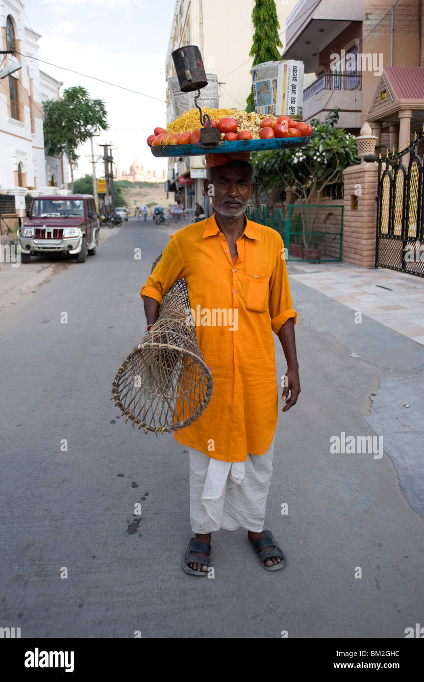 Dans l'homme kurta jaune avec le bac d'en-cas sur sa tête et le tableau sous son bras, pour les vendre au marché, Jodhpur, Rajasthan, India Banque D'Images