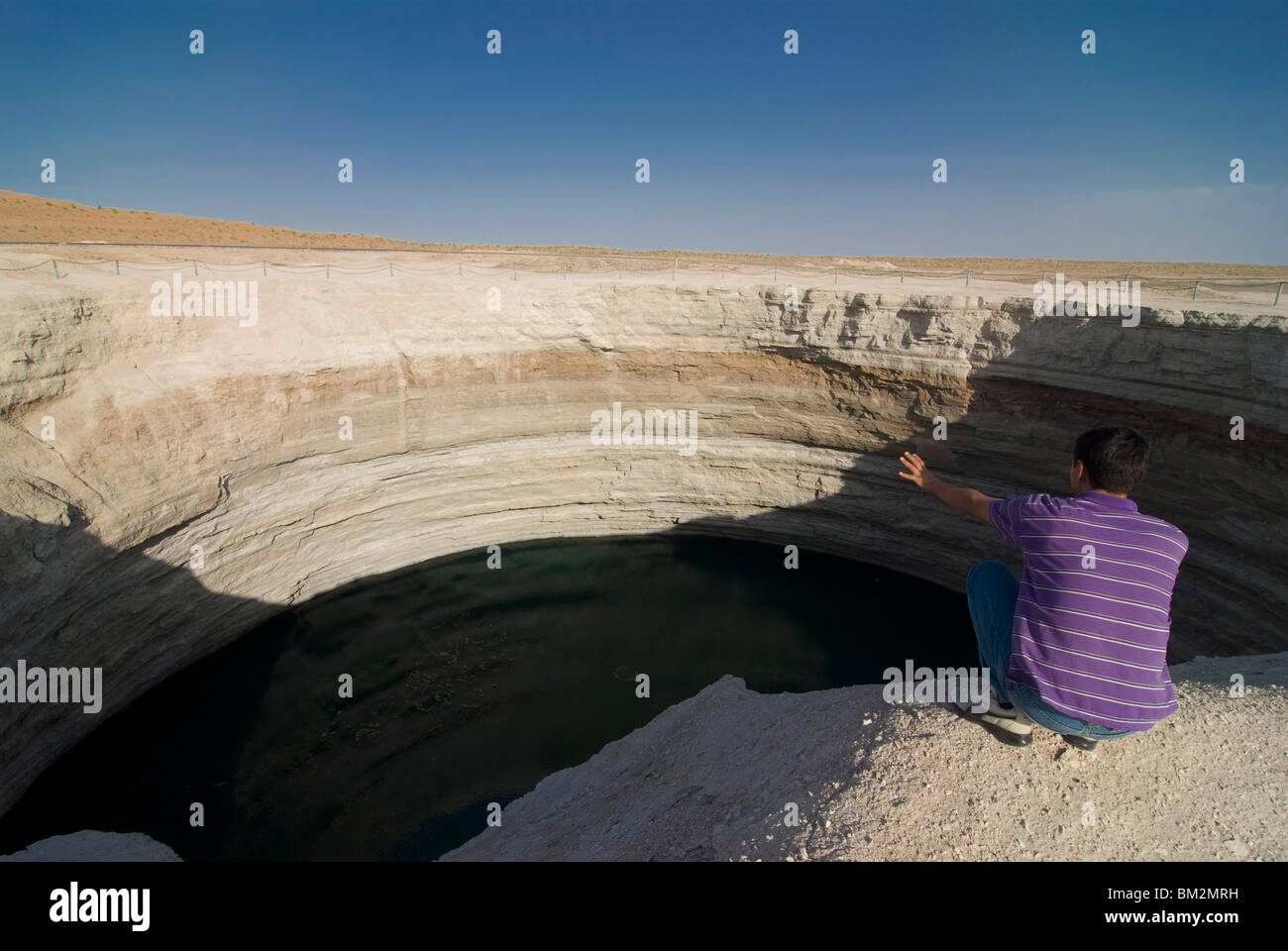 Homme assis sur le dessus d'un cratère rempli d'eau, désert de Karakol, le Turkménistan Banque D'Images