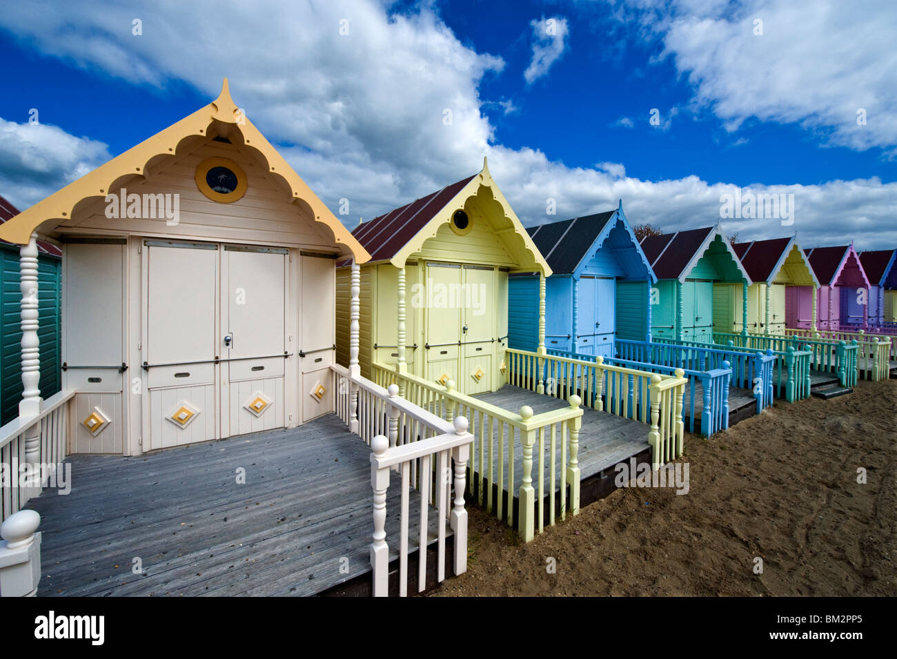 Une rangée de cabines colorées contre un ciel bleu au bord de la mer, sur une plage de sable sur l'Est de l'Essex MERSEA Island UK Banque D'Images