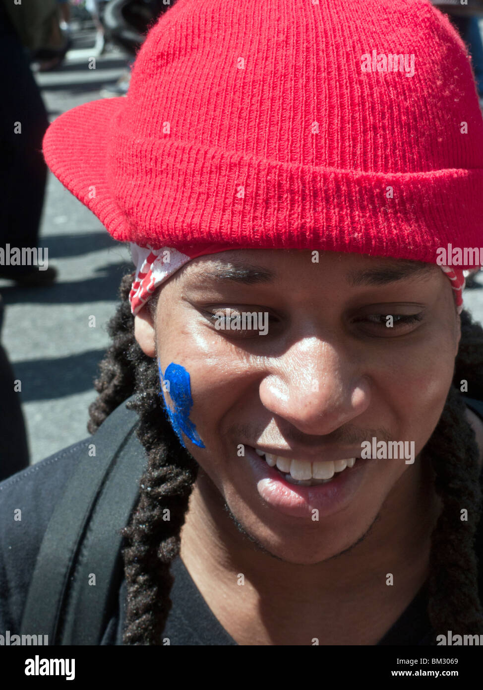 Teenage boy smiling black rouge vif en cap & dreadlocks avec papillon bleu peint sur sa joue au 9e Avenue Food Festival Banque D'Images
