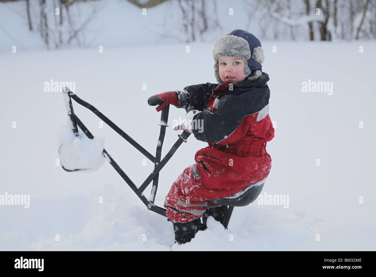 GARÇON TOUT-PETIT ASSIS SUR LA GRUE JOUET DANS LA NEIGE PROFONDE DE L'HIVER : un enfant de bébé garçon de deux ans joue avec la pelleteuse dans le modèle de parc de neige profond libéré Banque D'Images