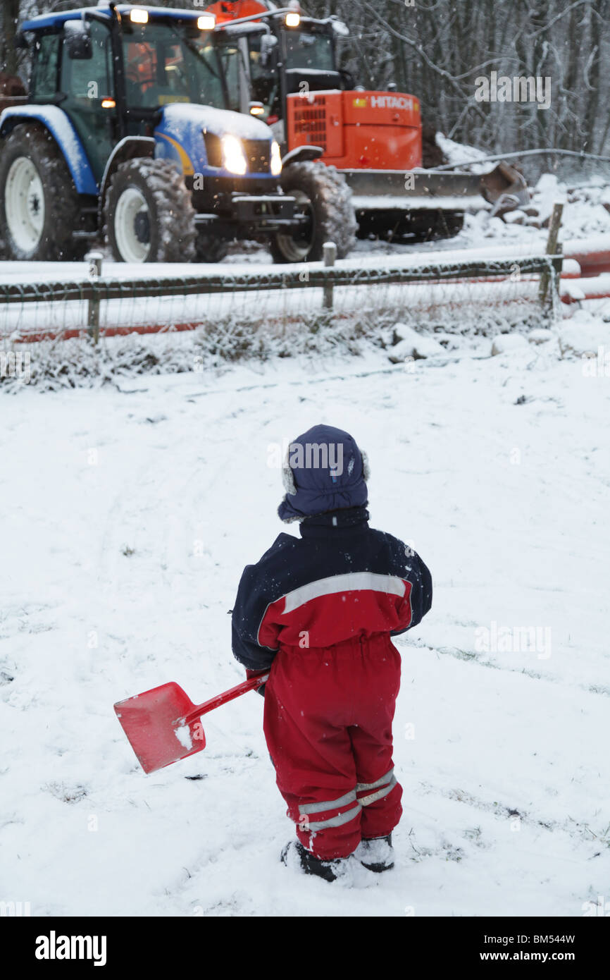LES TOUT-PETITS JOUENT EN FINLANDE LA NEIGE PROFONDE DE L'HIVER : un enfant de bébé garçon de deux ans joue avec un jouet pelle à bêche dans le modèle de tracteur de pelle à neige libéré Banque D'Images
