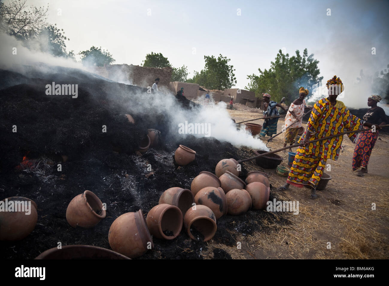 Les femmes au Mali retirer de l'utilisation de fours à bois accrochées. Les pots sont immédiatement plongé dans un mélange de petits fruits à l'eau. Banque D'Images