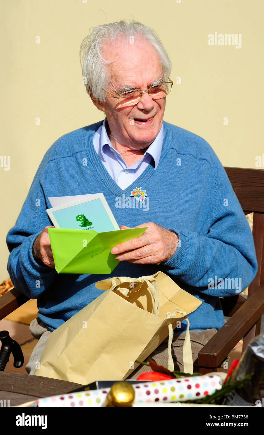 Un homme de rire comme il ouvre un dessin de carte d'anniversaire à l'occasion de son 90ème anniversaire (un anniversaire badge est épinglé sur son chandail). Banque D'Images