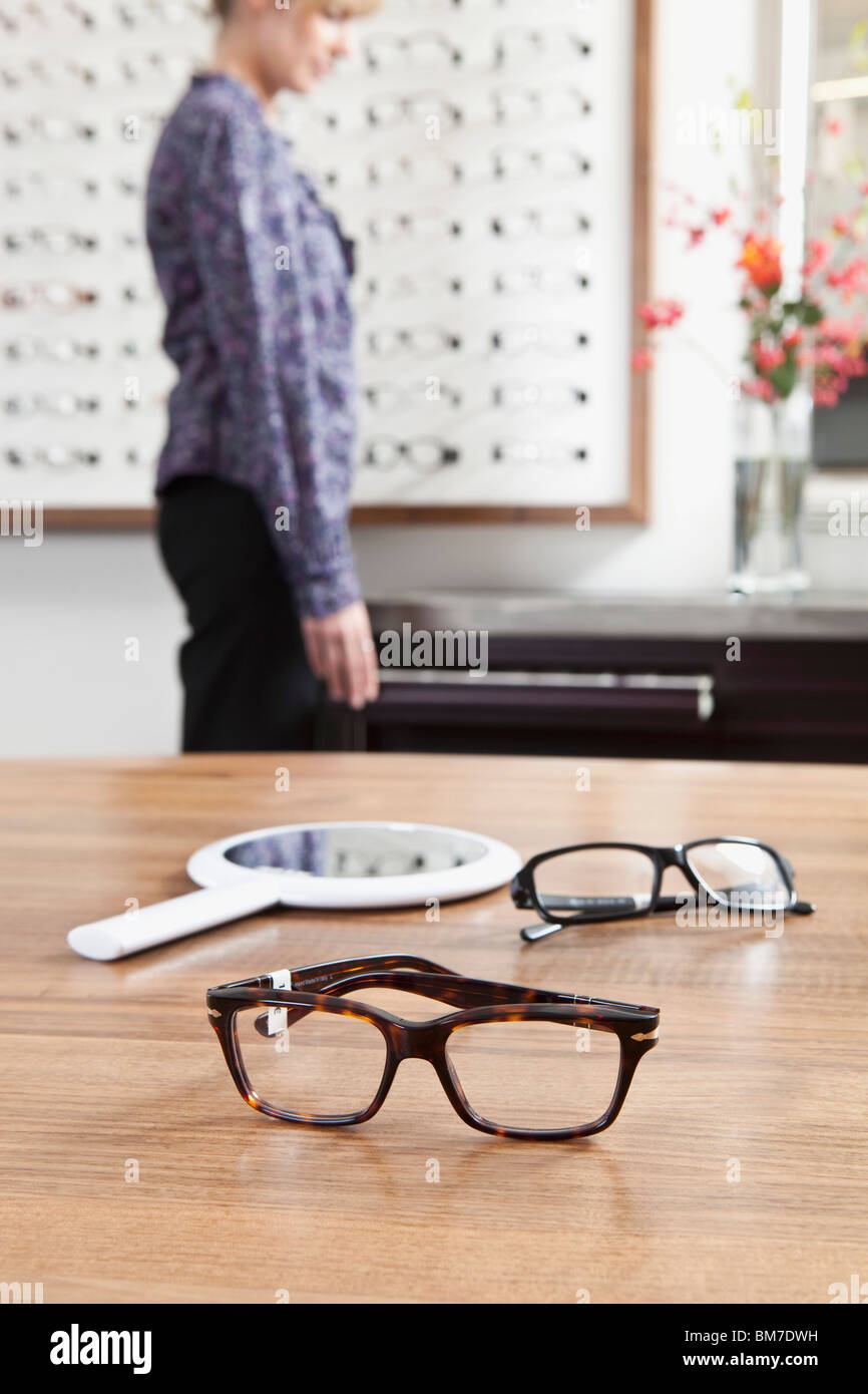 Deux paires de lunettes (une en focus) dans un magasin de lunettes, woman in background Banque D'Images