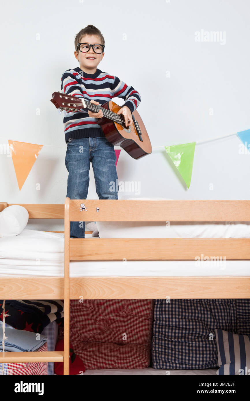 Un garçon debout sur un lit superposé joue avec une guitare Banque D'Images