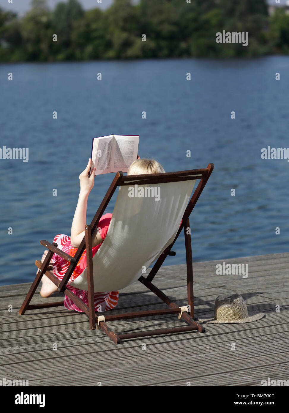 Une femme lisant dans une chaise de plage chaise longue sur un quai Banque D'Images