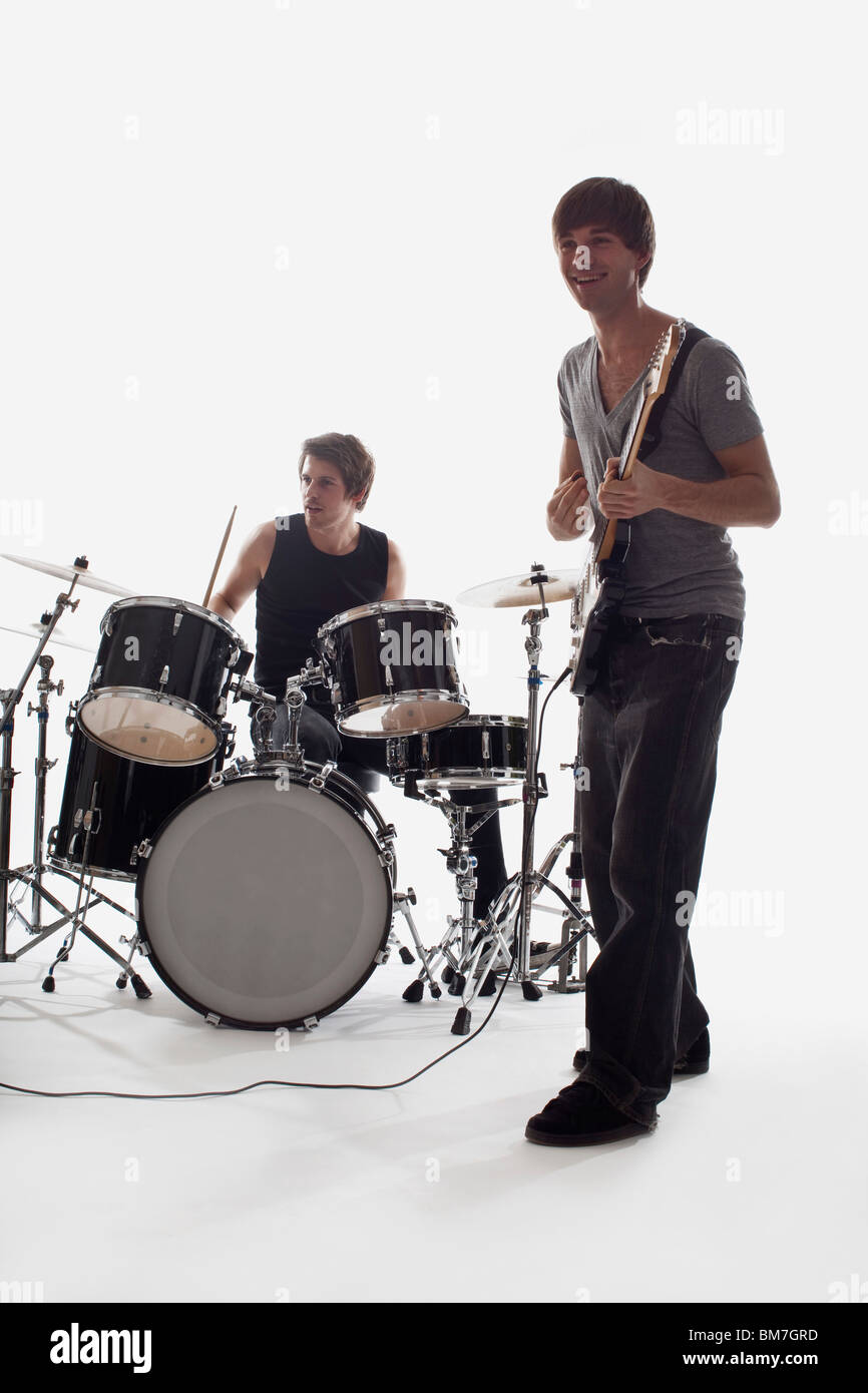 Un homme jouant de la guitare électrique et un homme à la batterie d'effectuer, studio shot, fond blanc, éclairage arrière Banque D'Images