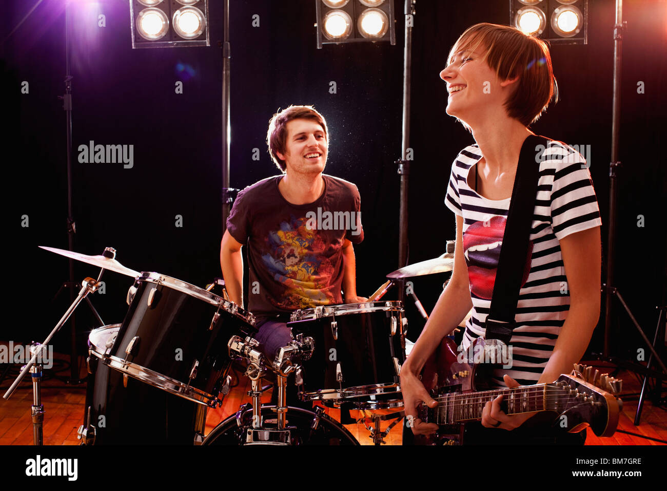 Un homme à jouer de la batterie et d'une femme qui joue de la guitare dans un groupe de rock sur scène Banque D'Images