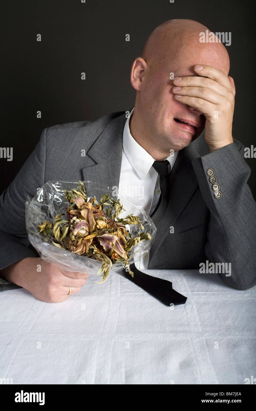 Un homme bien habillé tenant un bouquet de fleurs mortes et de pleurer Banque D'Images