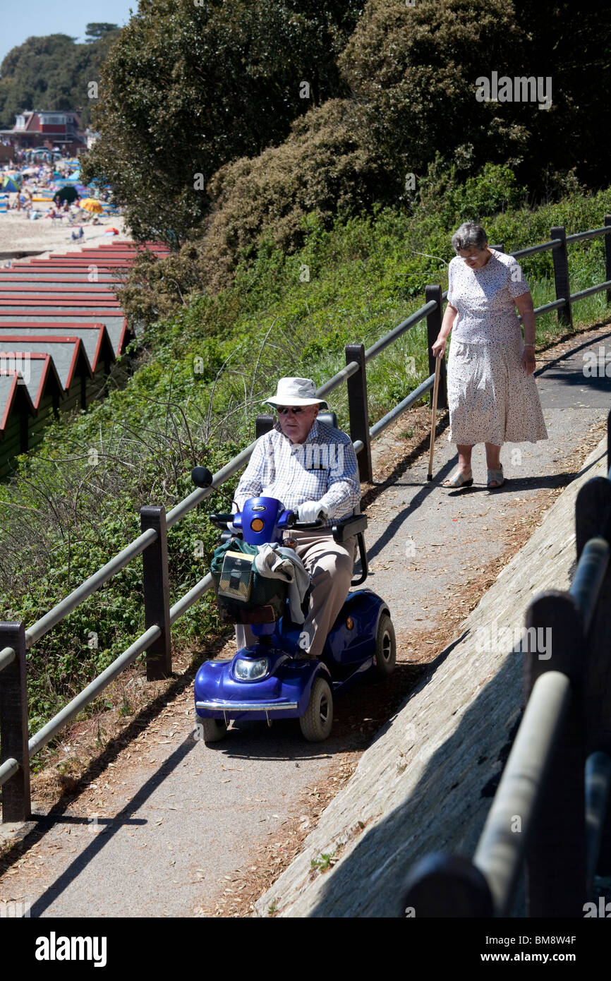 Vieux monsieur en chapeau de soleil sur la mobilité motorisée buggy suivie de large avec bâton de marche en descendant la bretelle vers beach Banque D'Images