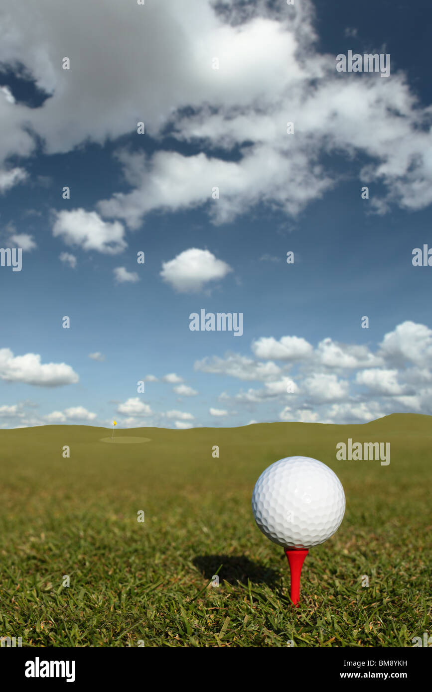 Balle de Golf sur tee vert et rouge avec drapeau dans la distance Banque D'Images