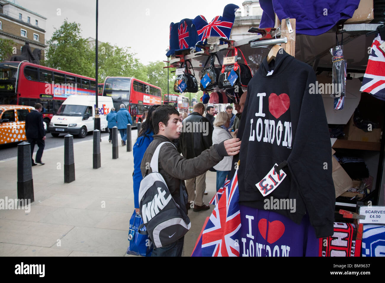 Un touriste examine les articles en vente sur un étal de souvenirs sur Whitehall, Londres, Angleterre. Banque D'Images