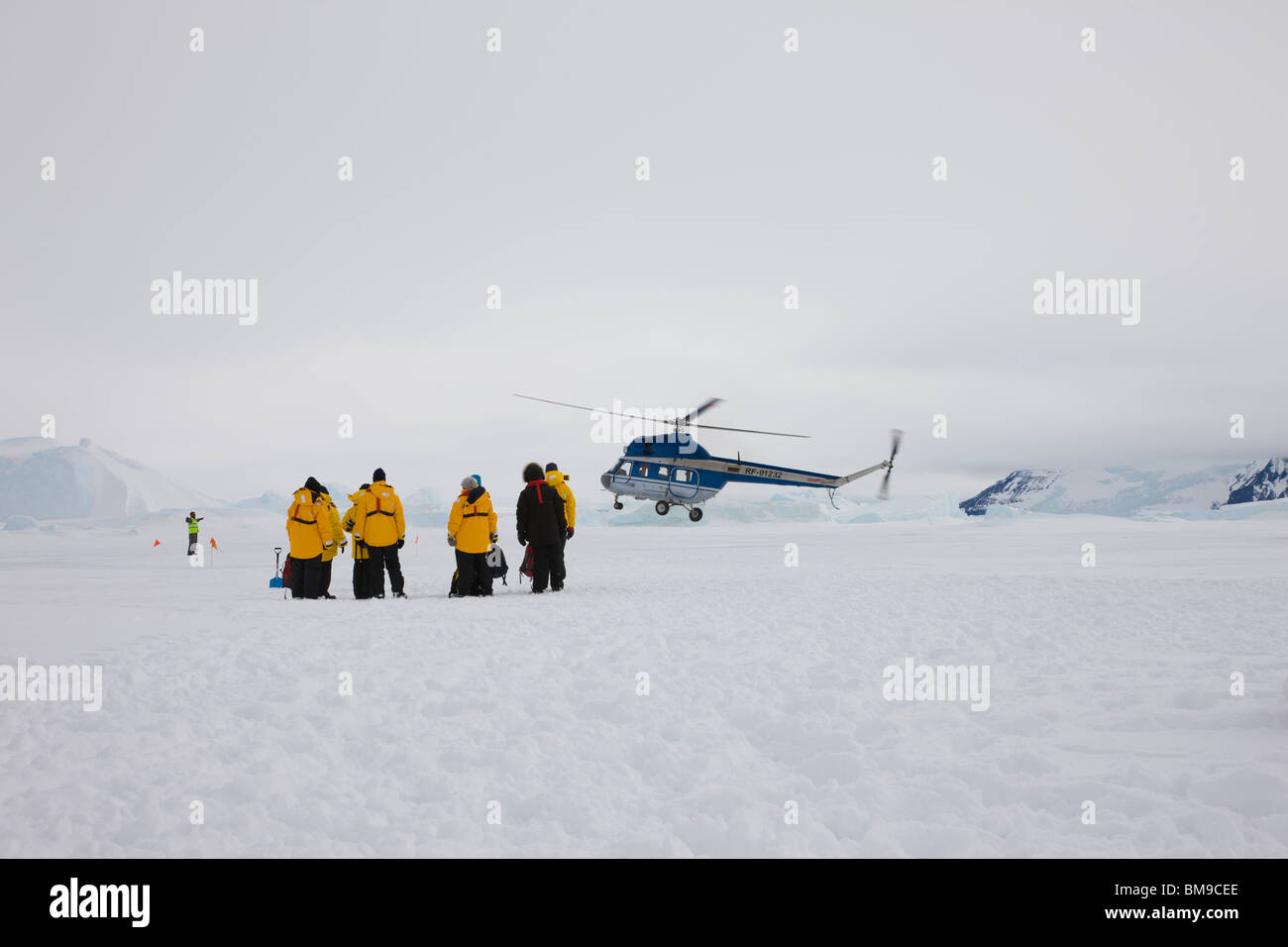 Hélicoptère à l'atterrissage sur la glace et de la neige en Antarctique, Snow Hill touristes portant des manteaux jaune en premier plan les glaciers en arrière-plan un ciel couvert Banque D'Images