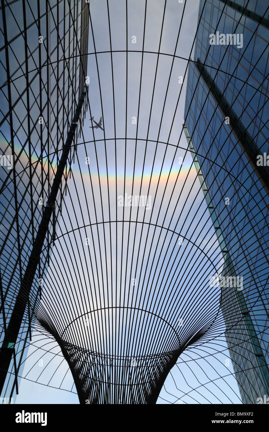 Un avion vole dans un arc-en-ciel circulaire dans le ciel au-dessus de London Docklands vue par un fil à l'extérieur de la sculpture KPMG L'AC. Banque D'Images