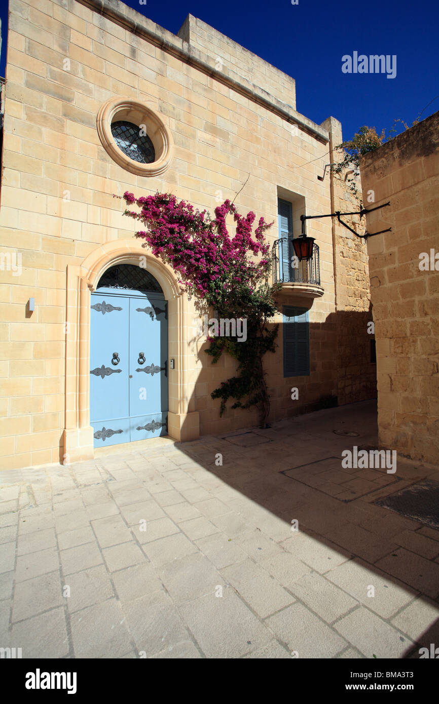 Une petite place dans la ville de Mdina, Malte. Une porte bleue et la floraison Bougainvillia. Ci-dessus est une fenêtre ovale Banque D'Images