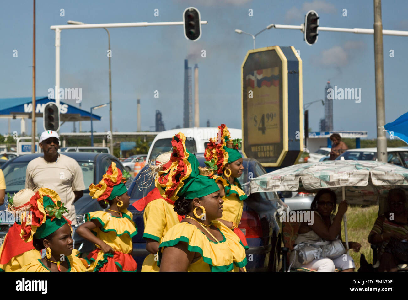 Les participants dansent dans Harvest Festival Parade avec la pollution de l'ISLA raffinerie de pétrole dans l'arrière-plan, Curacao, Antilles néerlandaises Banque D'Images