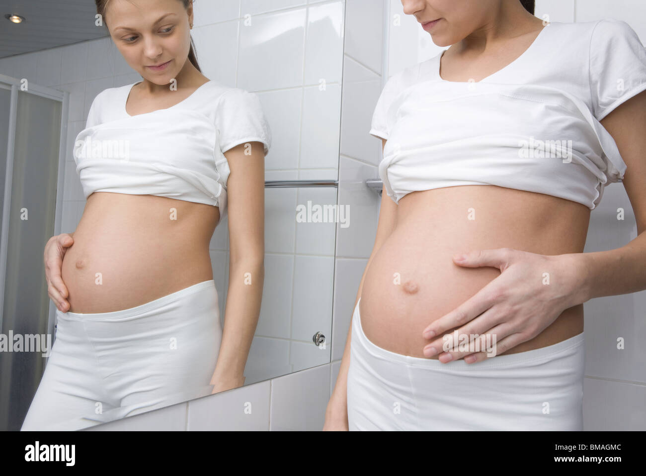 Femme enceinte se tient à l'estomac en miroir de salle à Banque D'Images