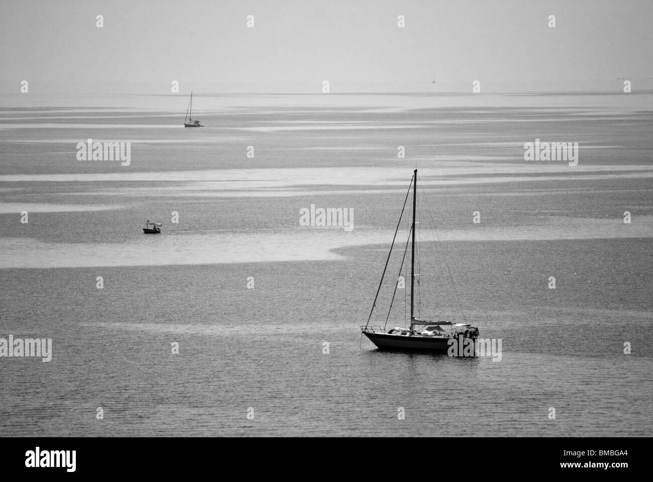 Une image en noir et blanc de deux voiliers et un bateau de pêche naviguant dans la mer ionienne (Corfou, Grèce) contre l'horizon clair. Banque D'Images