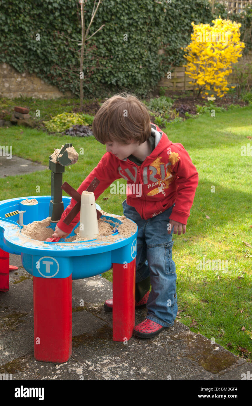 Quatre ans Garçon jouant avec le sable bac à sable dans le jardin arrière Banque D'Images
