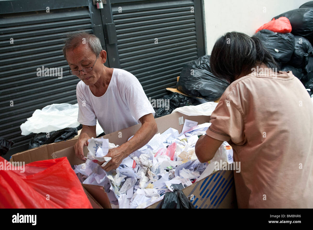 Un couple de personnes âgées à trier les déchets de papier de recyclage dans une ruelle à Singapour Banque D'Images