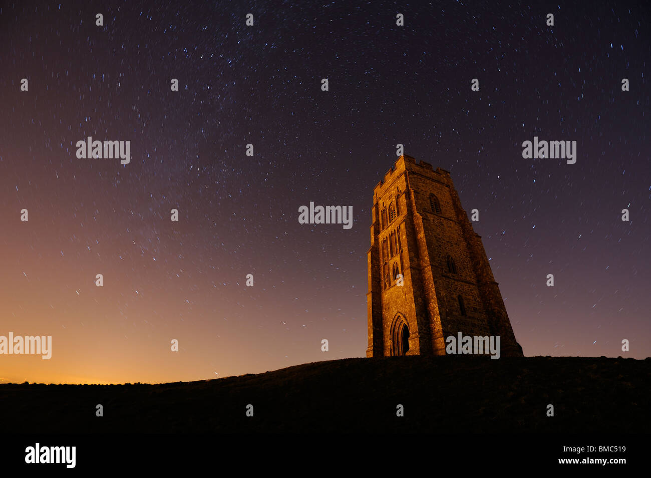 Glastonbury Tor allumé par la pollution lumineuse et avec un ciel étoilé derrière elle. Banque D'Images