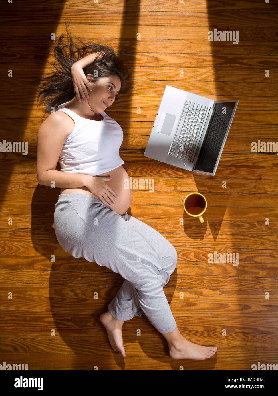 Vue de dessus d'une jeune femme enceinte se trouvant sur le plancher avec un ordinateur portable et d'une tasse de thé. Banque D'Images