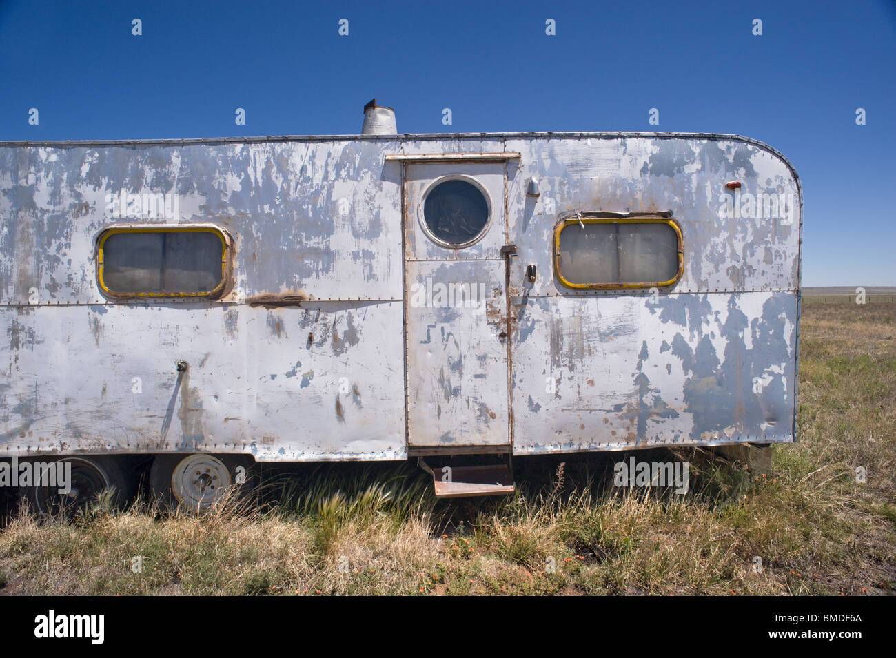 Une vue fréquente au Nouveau Mexique - une peinture-peeling, bosselé, de l'épave remorque camping assis dans une mauvaise herbe-patch - Encino, Nouveau Mexique. Banque D'Images