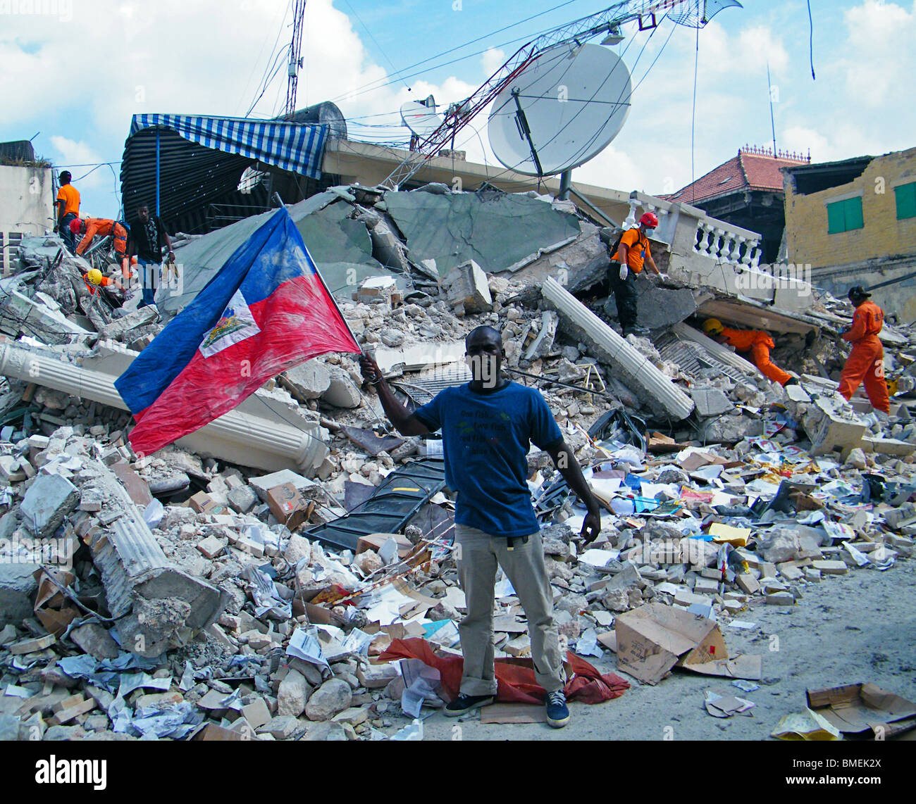 Un homme agite les drapeau haïtien à Port-au-Prince et les équipes de recherche et de sauvetage Recherchez les décombres pour les survivants du séisme en Haïti de Banque D'Images