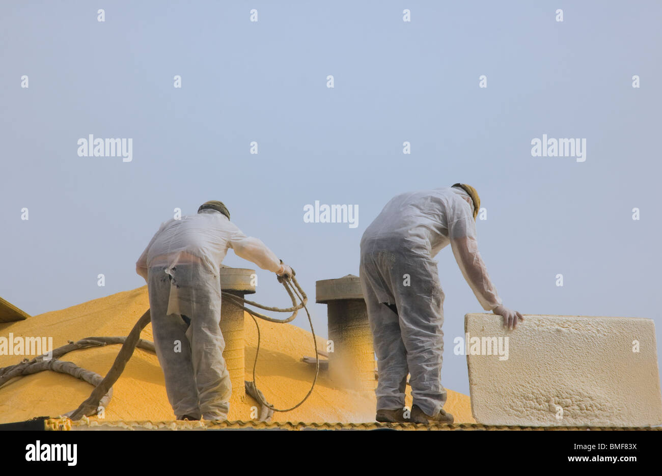 Ouvriers pistolage le toit d'un bâtiment avec peinture jaune. Banque D'Images