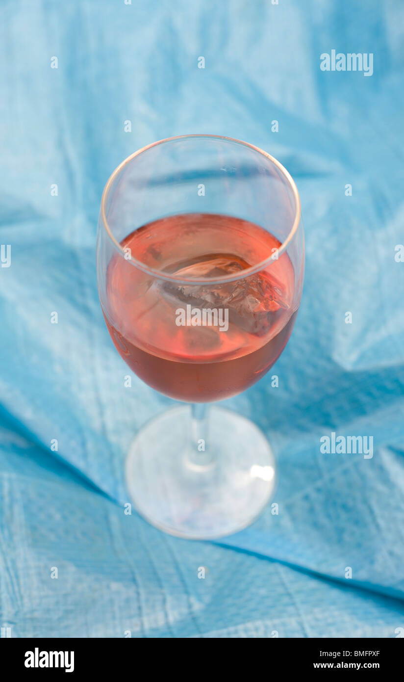 Un verre de vin rose avec un cube de glace sur un fond bleu. Banque D'Images