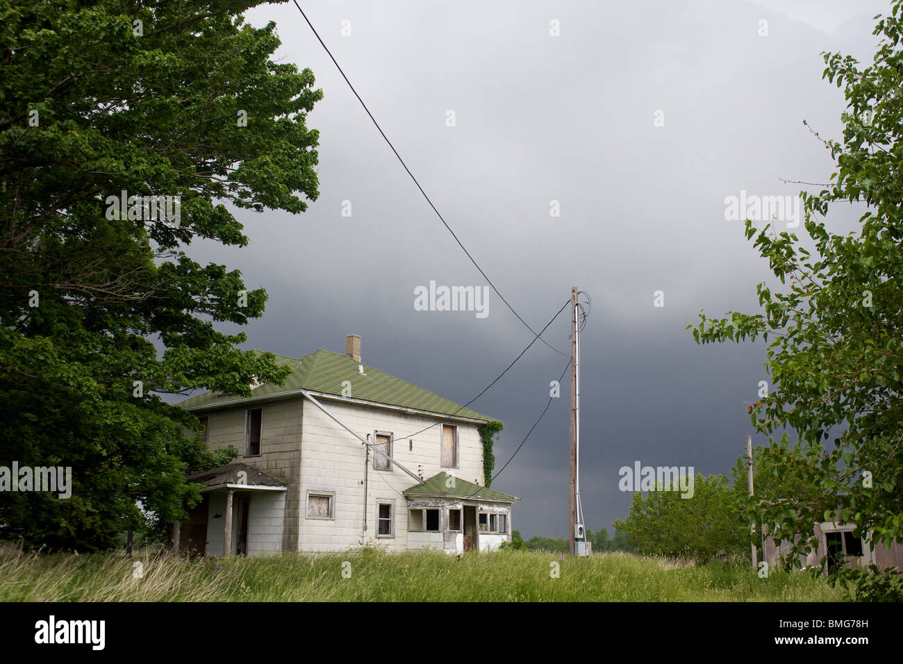 Une vieille ferme abandonnée, vandalisée, conciliabules chambre à côté d'un grand arbre que les vents de whip et de sombres nuages en rouleau Banque D'Images