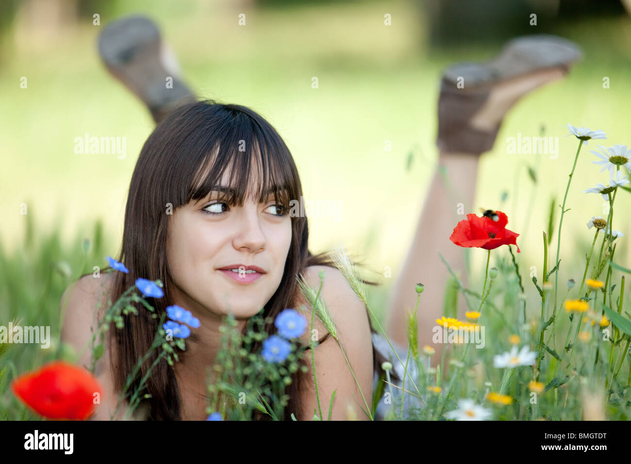 Beautiful teenager girl lying in flower bed à bumblebee on poppy Banque D'Images