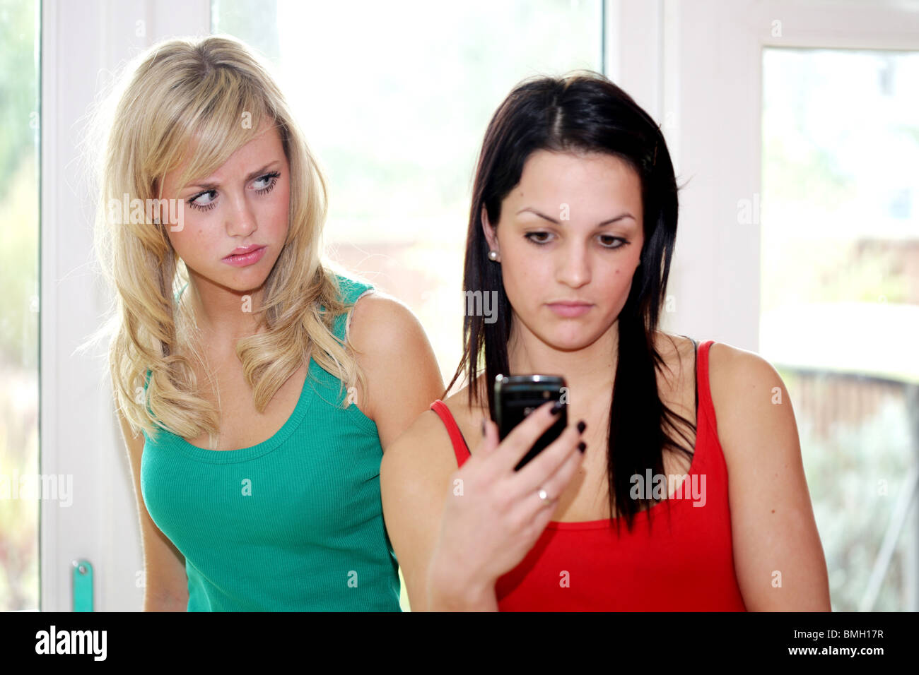Teenage girlfriends en utilisant un téléphone mobile modèle publié. Banque D'Images
