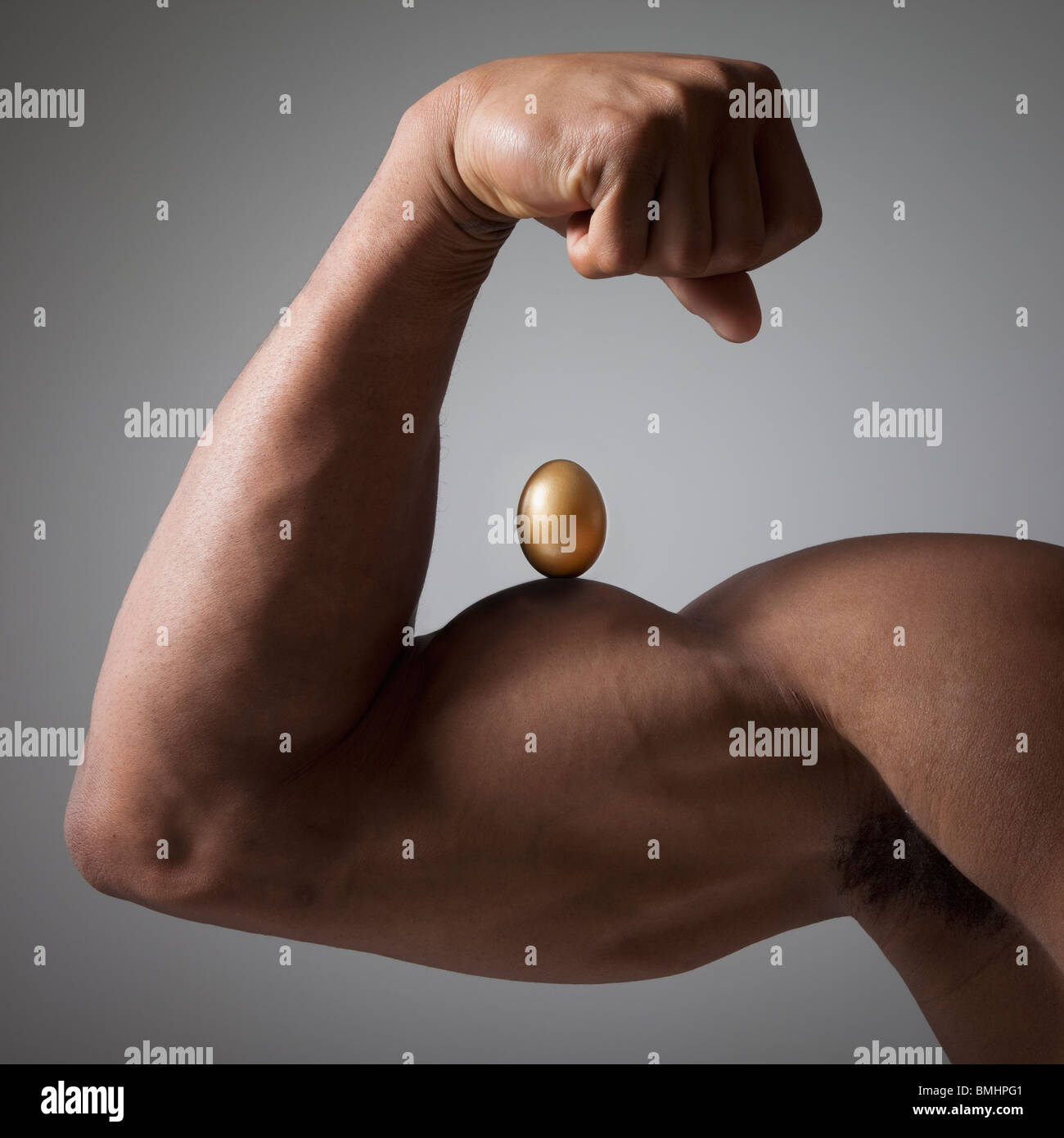 Œuf d'or perché sur un bras musclé fléchie Banque D'Images