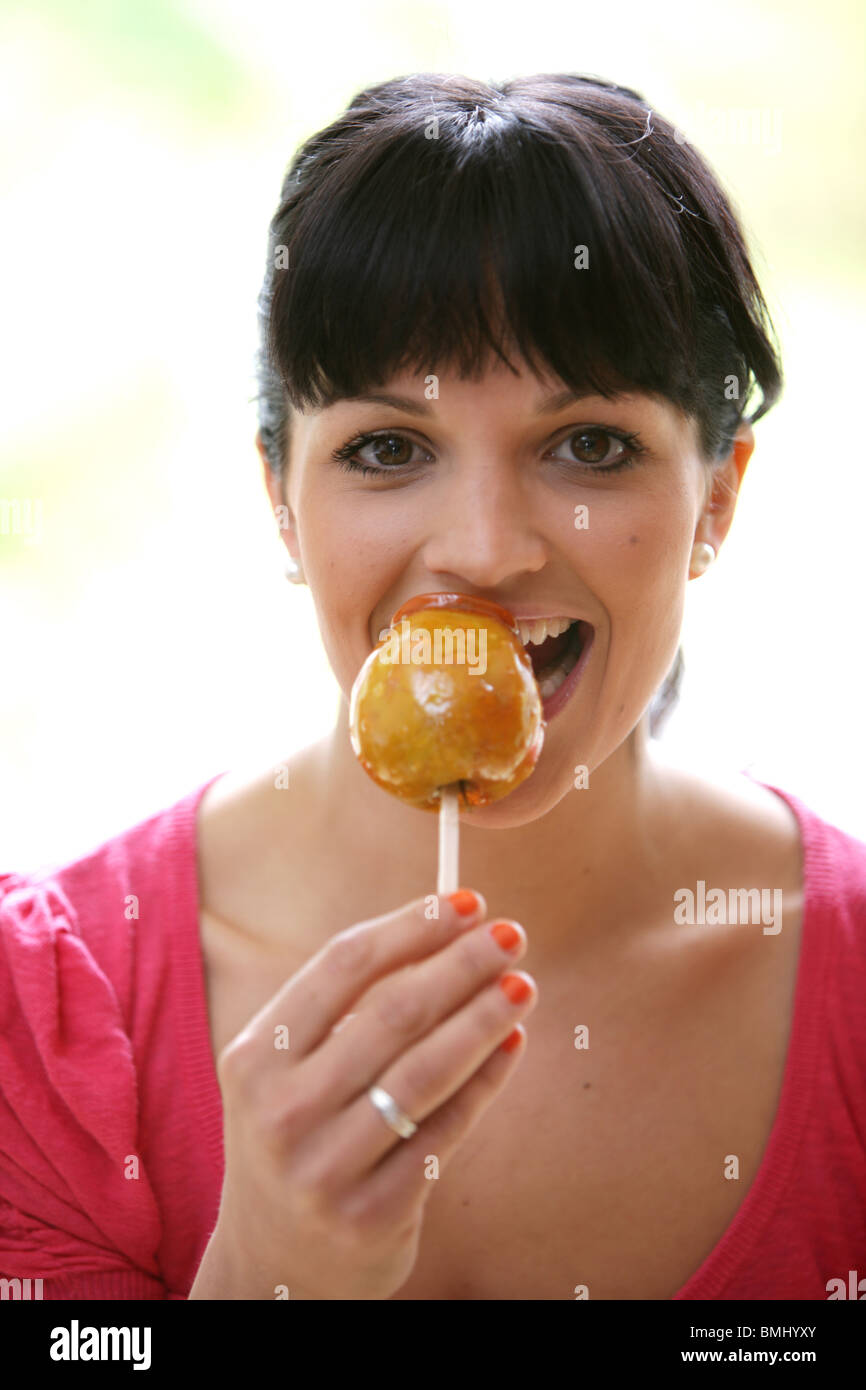 Jeune femme mangeant une pomme caramel. Parution du modèle Banque D'Images