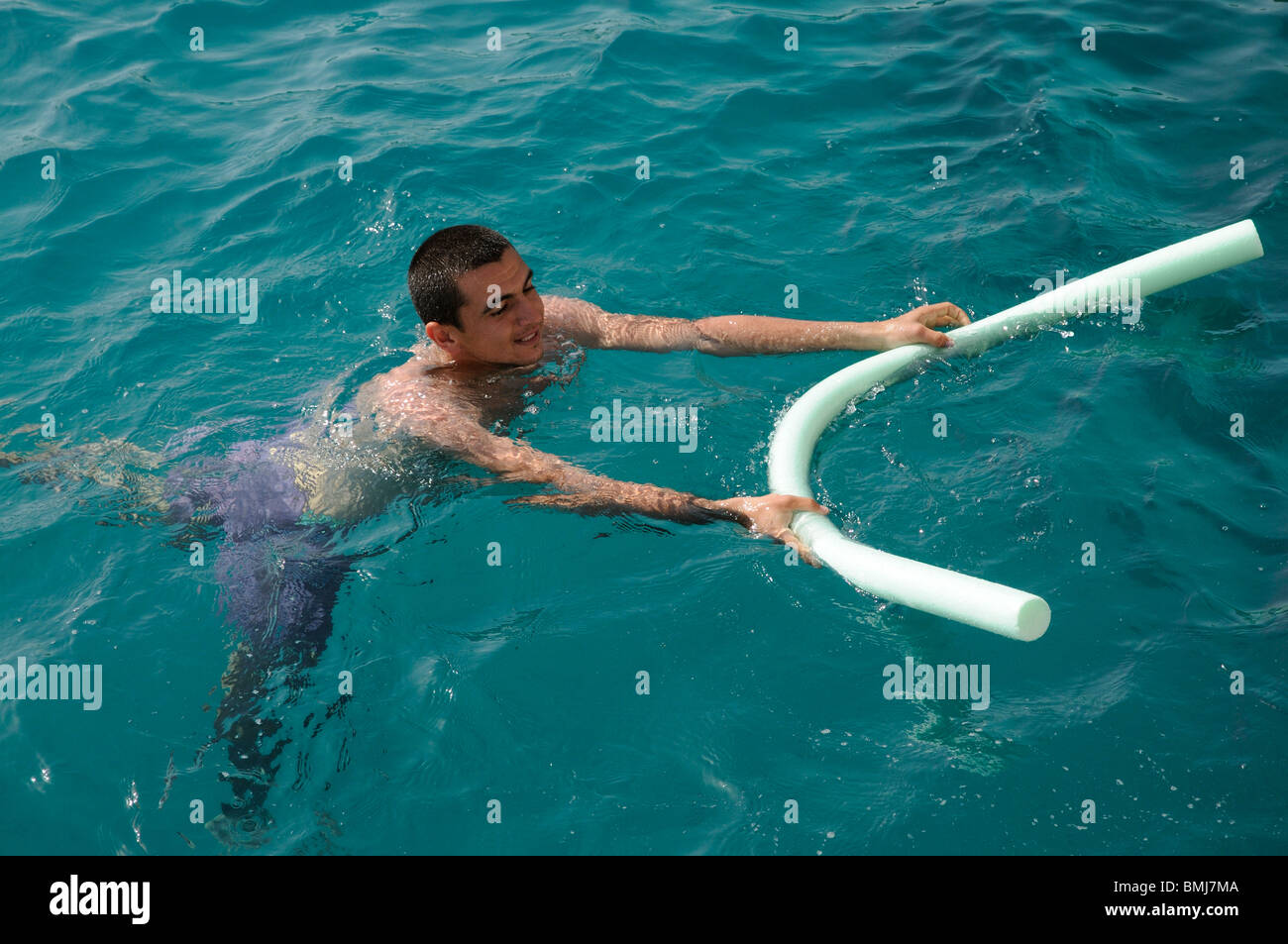 Jeune homme à l'aide d'une piscine et nouilles comme une aide à la flottabilité il flotte dans la mer Banque D'Images