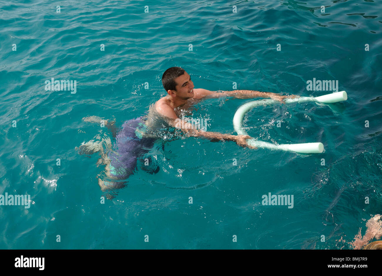 Jeune homme à l'aide d'une piscine et nouilles comme une aide à la flottabilité il flotte dans la mer Banque D'Images