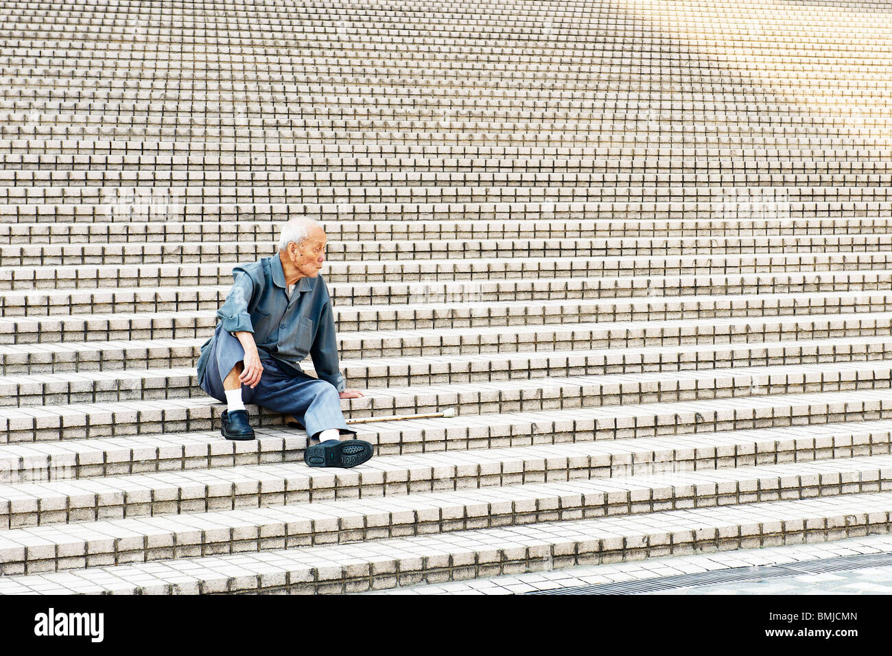 Un vieux solitaire chinois est assis à l'ombre sur les mouches de escaliers en dehors de Hong Kong Art Centre, regarde void motionlessly. Banque D'Images